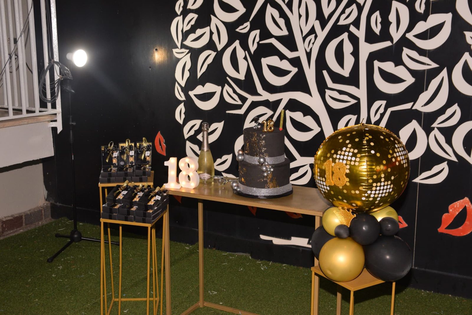 Sweet table davanti al muro dell'albero dei baci con torta nera e oro e numeri luminosi 18