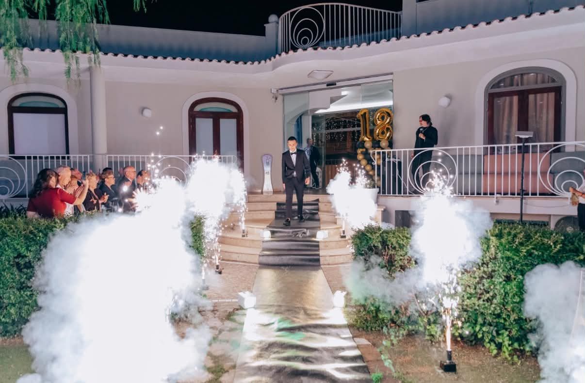 Ingresso della villa di sera tra fuochi freddi e fumo scenico