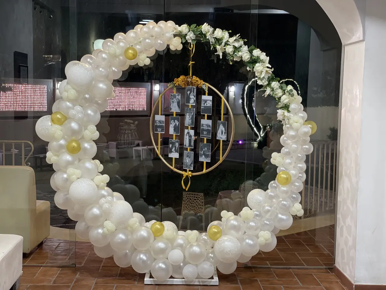 Allestimento circolare con palloncini bianchi e oro, fiori e fotografie per un evento