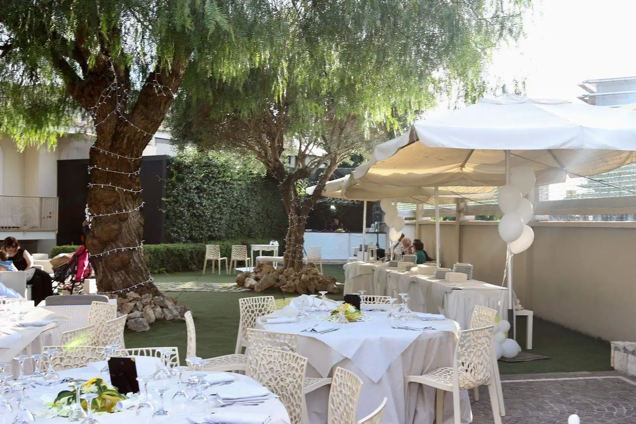 Veduta del giardino con alberi, tavoli apparecchiati e buffet sotto gli ombrelloni bianchi