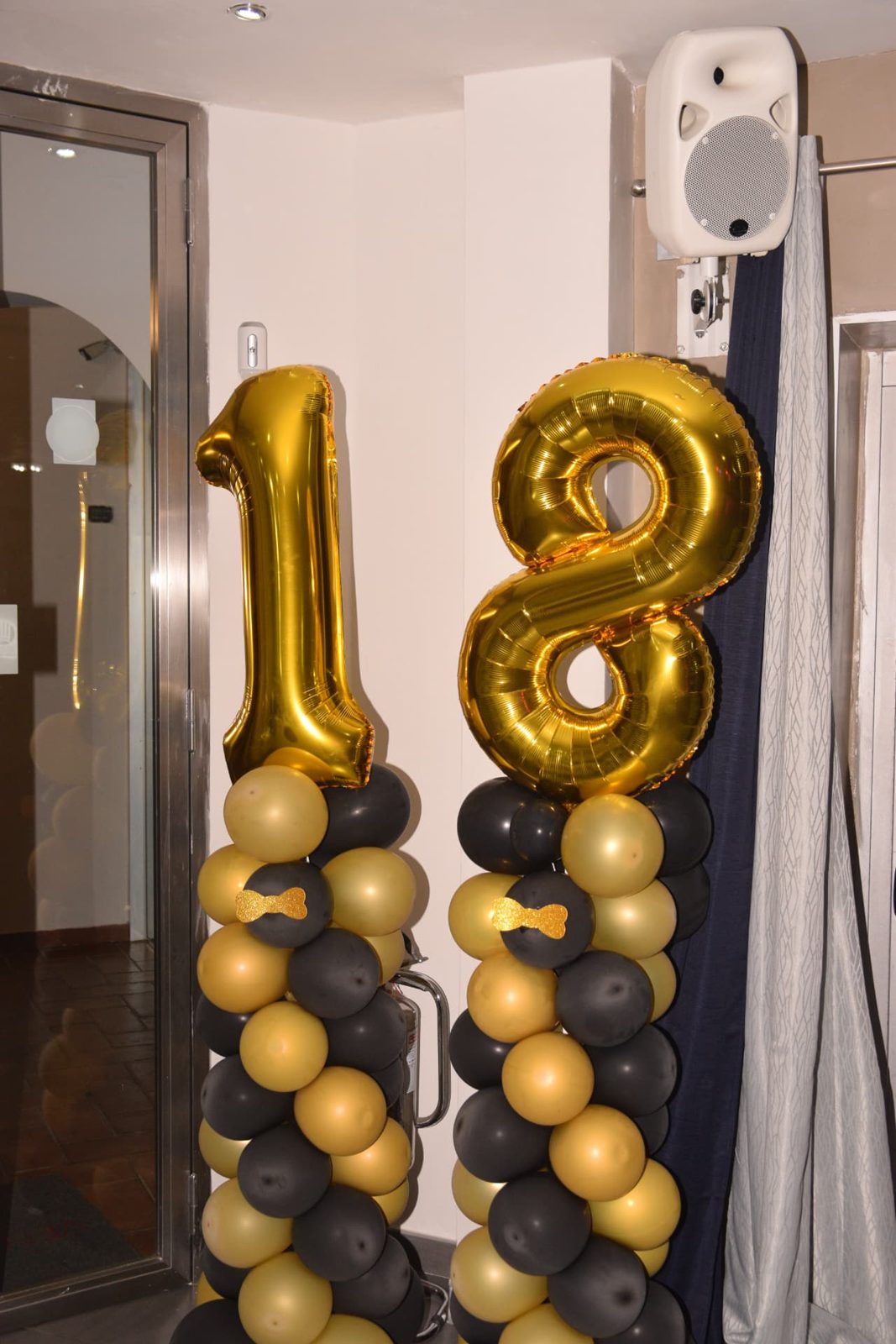Colonne di palloncini nero-oro con numeri 18 dorati all'ingresso